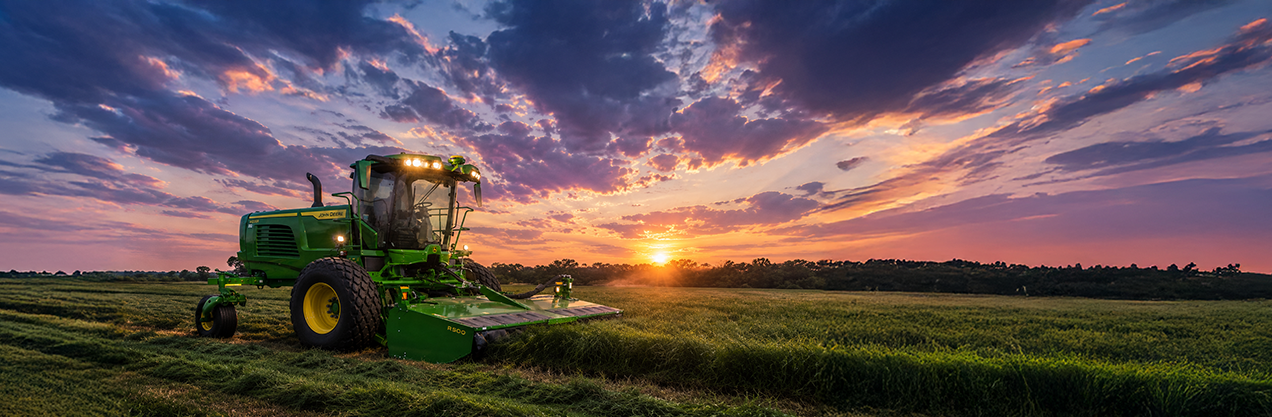 John Deere W235R windrower harvesting Coastal Bermuda hay at dusk